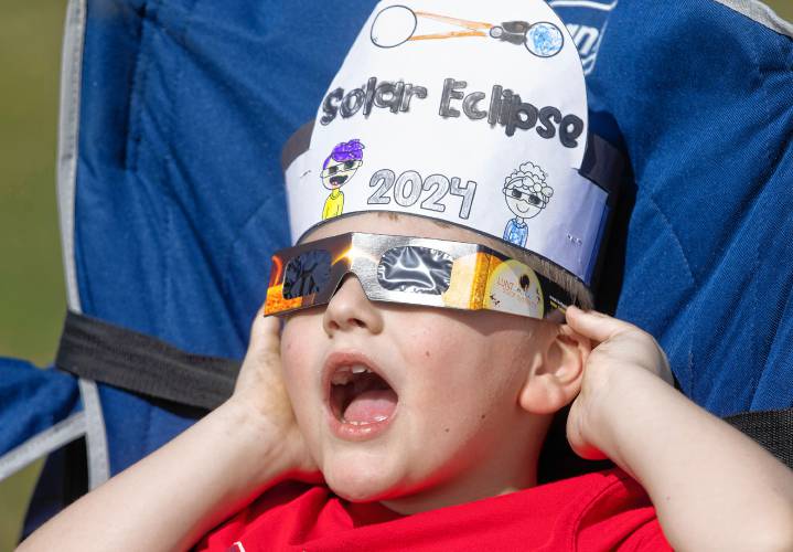 Axel Laperle, 6, looks up at the eclipse in the middle of a soccer field on the campus of NHTI in Concord with his cousin, Logan Lavoie and his grandparents, Lynn and Douglas Laperle as the light dimmed and it reached the maximum coverage on Monday, April 8, 2024.