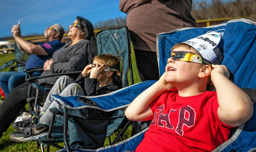 Axel Laperle (right), 6, looks up at the eclipse in the middle of a soccer field on the campus of NHTI in Concord with his cousin, Logan Lavoie and his grandparents, Lynn and Douglas Laperle as the light dimmed and it reached the maximum coverage on Monday, April 8, 2024.