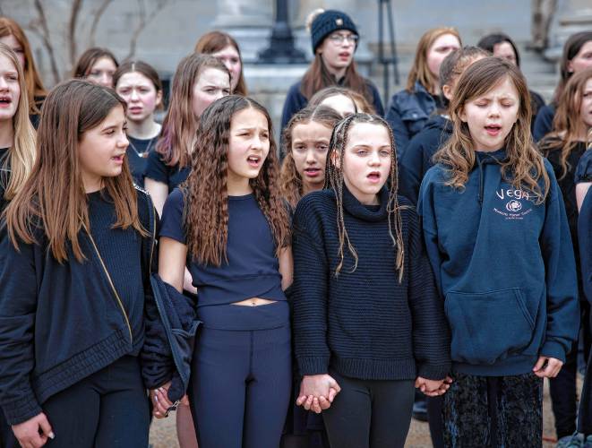 Weare Middle School choir members Addison Crete (left), Skylynn Bishop, Maya Peterson and Addie Lussier all hold hands while singing in front of the State House on Wednesday, March 27, 2024 for Music in our Schools Month proclaimed by Governor Chris Sununu.