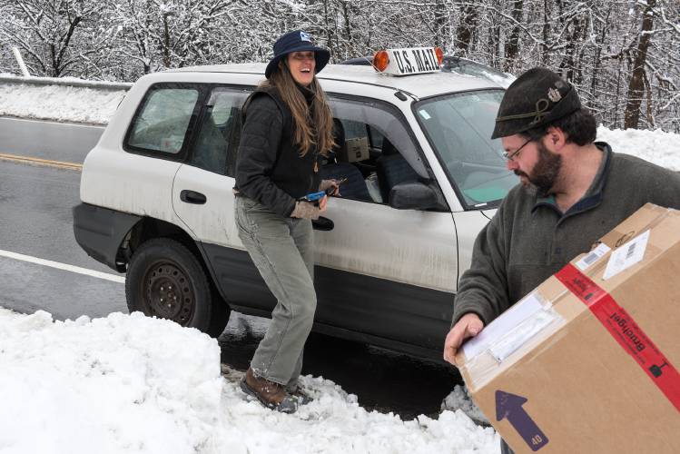 Mail carrier Jennifer Brown, left, leaves a package with Maurizio Odermatt, right, at his home in Vershire during a power outage earlier this month. Brown said that even though it's the busiest time of year, she enjoys working during the holidays because people are happy to see her when she brings their packages. 