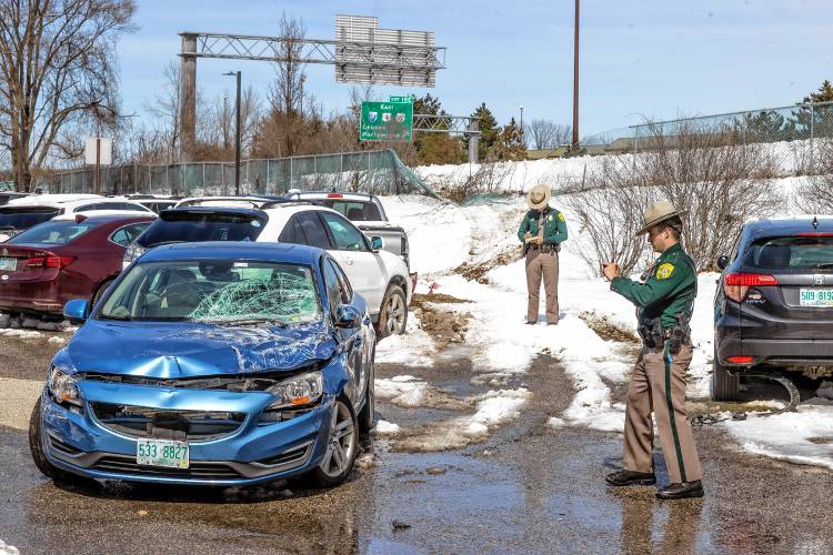 State police officers work on reports after a Redimix cement truck slid off I-93 South, broke through a fence (seen in background) and hit numerous vehicles parked in the Concord Coach Lines lot on Stickney Avenue.