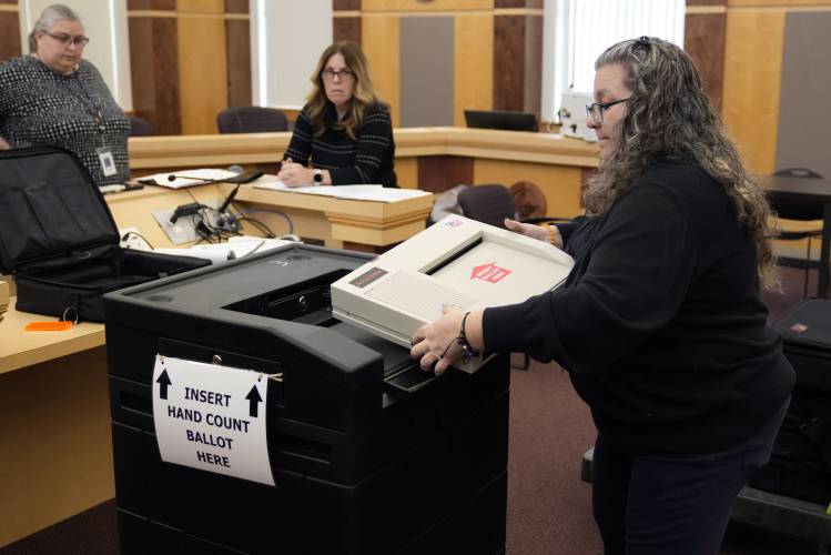 Lisa Hultgren, the Derry, N.H. town moderator, loads a vote counting machine into a cart, which stores the paper ballots, while testing vote counting machines before the New Hampshire primary at the Derry Municipal Center, Tuesday, Jan. 16, 2024. At left is Tina Guilford, Derry town clerk and at center is Lynne Gagnon, Derry deputy town clerk. (AP Photo/Charles Krupa)
