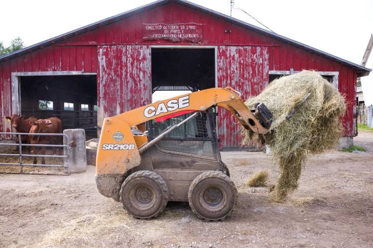 Kevin Morrill uses a loader to move a round bail of hay to feed cows on the farm on June 26, 2025.