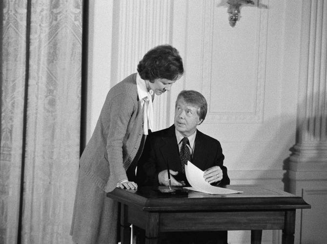 FILE - President Jimmy Carter talks with his wife, first lady Rosalynn Carter, prior to signing an executive order establishing a Presidential Commission on Mental Health, Feb. 17, 1977, in the East Room of the White House in Washington. Health care experts say the advocacy of Rosalynn Carter, who died Sunday, Nov. 19, 2023, at age 96, created a framework for much of the progress on mental illness in America. (AP Photo/Charles Tasnadi, File)