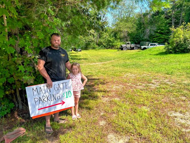 Justin Dearborn with his 7-year-old daughter, Jemma, at the front of their yard in Hopkinton with signs preparing to open their yard for parking for fairgoers