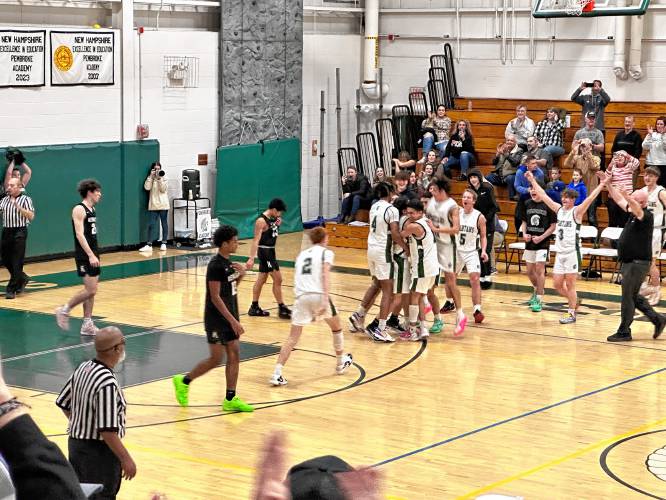 The Pembroke Academy boys’ basketball team surrounds and celebrates with Joe Fitzgerald after reaching his 1,000th career point on Friday on his home court. Fitzgerald scored 35 points for the Spartans in a 77-45 victory over Kennett.