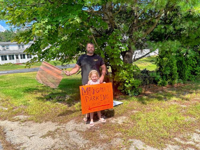Justin Dearborn with his 7-year-old daughter, Jemma, at the front of their yard in Hopkinton with signs preparing to open their yard for parking for fairgoers