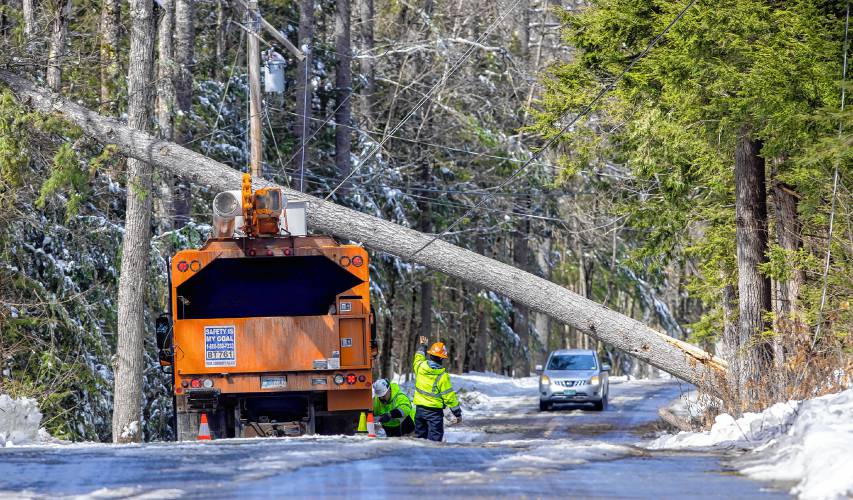 A tree service worker warns a car as they wait for Eversource crews to come and ground wires on Dustin Road in Hopkinton on Monday.