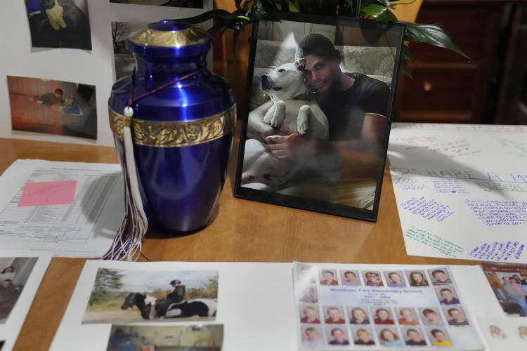 Family photographs of Zach Robinson, including one of him embracing his dog, Ziva, are displayed on the dining room table next to an urn containing his remains, during an interview at his family's home, Thursday, Nov. 30, 2023, in Dover, N.H. Robinson spent decades trying to fight off nightmares about being raped as a child at New Hampshire’s youth detention center. He died last in November, still waiting for accountability for his alleged abusers. (AP Photo/Charles Krupa)