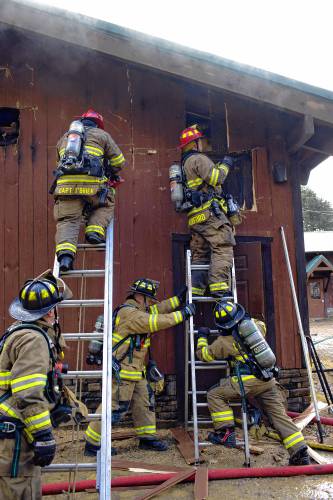 Firefighters vent the roof of the Carter Lodge at the Hidden Valley Scout Camp in Gilmanton on Monday. The smoky fire at the isolated camp went to two alarms and drew fire companies from around the area.