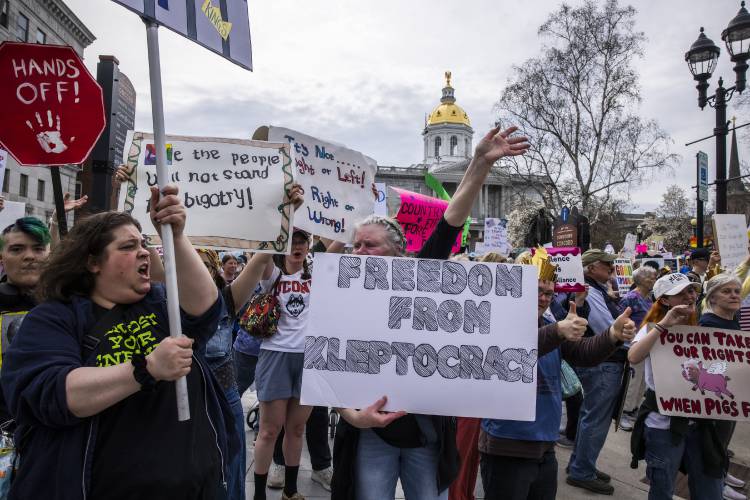 Protesters call out to the cars passing on downtown Main Street during the ‘Hands Off’ protest in front of the State House on Saturday, April 19, 2025.