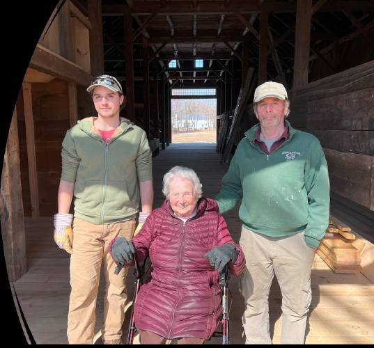Henrietta Kenney sits in her barn that was restored by Tim Andrews, Barns & Bridges of New England, on right, and his son Evan Andrews, who assisted on the project, to the left.  “Growing up on small local farms and given our love of local history, it was a life-long plan of my late husband Harold’s and mine to preserve this unique barn for future generations to learn about and enjoy for years to come,” said Kenney.