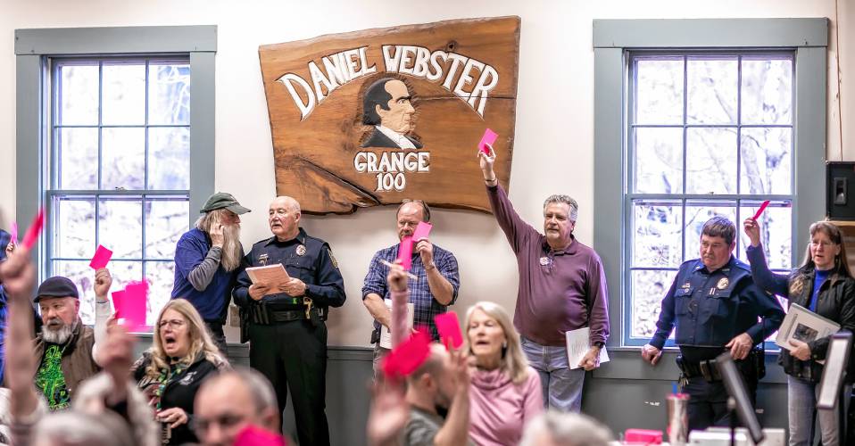 Webster residents raise their voting cards to pass an article on the warrant on Saturday.