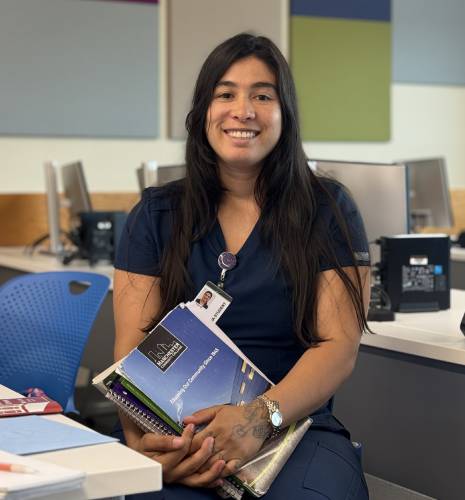 Lilian Gomez smiles and holds a few of her textbooks before her graduation from Second Start’s LNA for New American’s program. 