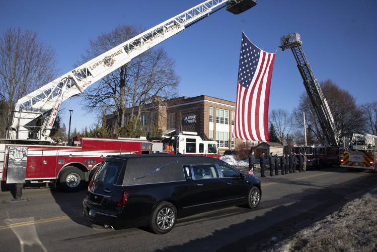 The hearse carrying Christopher Girard passes by a flag draped between two fire engines on its way to Bennett Funeral Home on Monday.