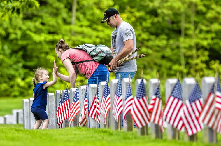 Riley Bell Prince, 3, helps plant American flags with her parents, Matt and Suzanne, at the New Hampshire Veterans Cemetery on Thursday, May 23, 2024. Sgt. Matt Prince served in Iraq for eight years and his father served in World War II. Veteran groups and citizens put flags on every marker.