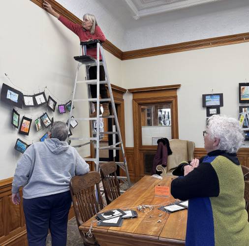 Henniker students were tasked with representing Azalea park and what it means to them through illustrations that now hang in the Tucker Free Library. Susan Adams stands in the foreground watching Kay Reynolds hang up artwork.