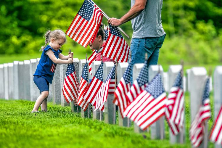 Riley Bell Prince, 3, helps plant American flags with her parents, Matt and Suzanne, at the New Hampshire Veterans Cemetery on Thursday, May 23, 2024. Sgt. Matt Prince served in Iraq for eight years and his father served in World War II. Veteran groups and citizens put flags on every marker.