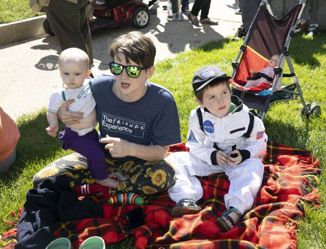 Danielle Vincent holds Maple Tyrrell, as Ollie Tyrrell, 6, sits in his space suit at the dedication of the Christa McAuliffe statue on the State House grounds on Monday.