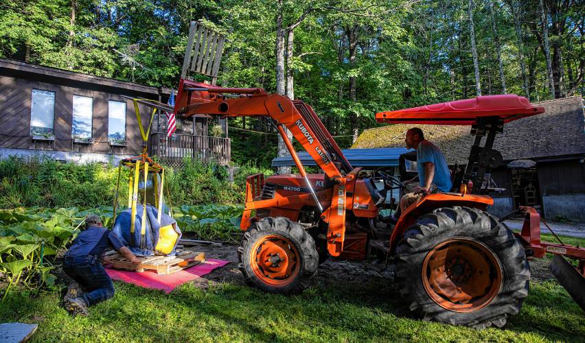 Nate Chartier guides John Lynch on his tractor as they put the giant pumpkin on a skid to transport it on Wednesday, August 28, 2024 so that they can deliver it to the Hopkinton Fair for judging.