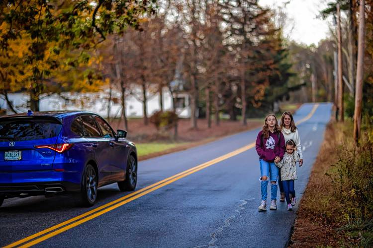 Abbie Teachout and her two young daughters, Piper (left) and Chloe, walk on New Rye Road in Epsom on their way to the kids’ bus stop as a car drives by on Thursday.