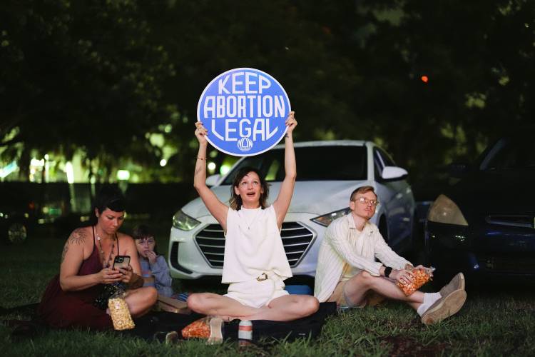 Reproductive rights advocate Kat Duesterhaus holds up a sign as U.S. President Joe Biden and his Republican rival, former President Donald Trump speak about abortion access, as the the first general election debate of the 2024 season is projected on a outdoor screen at the Nite Owl drive-in theater, Thursday, June 27, 2024, in Miami. (AP Photo/Rebecca Blackwell)