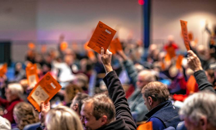 Bow residents raise their cards to approve an early warrant article during town meeting at Bow High School on Wednesday night.