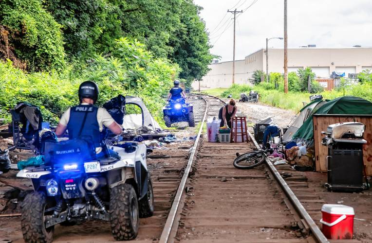 A homeless woman underneath the I-393 bridge gathers her belongings as Concord police on ATVs travel to the encampment in back of Robin Bach’s home on North Main Street on Tuesday. Police were going to clear out both areas.