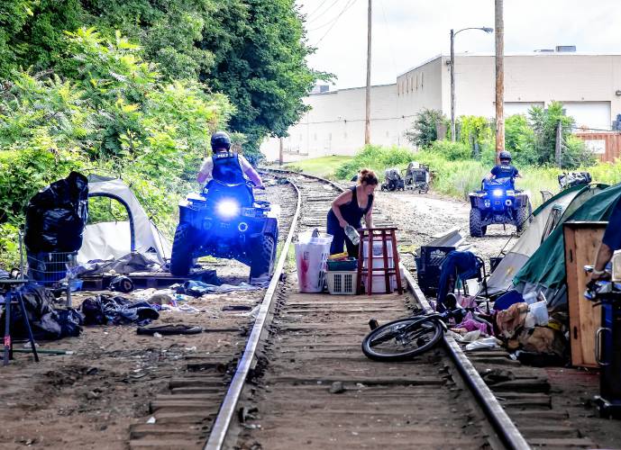 A homeless woman underneath the I-393 bridge gathers her belongings as Concord police on ATVs move around the tracks on their way to the encampment in back of Robin Bach’s home on North Main Street on Tuesday, July 23, 2024. The police were going to come back to the bridge area to clear that out as well.