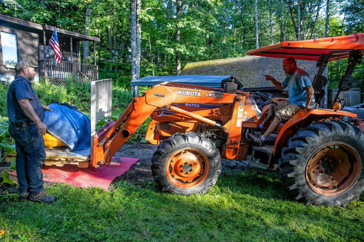 Nate Chartier guides John Lynch on his tractor as they put the giant pumpkin on a skid to transport it on Wednesday, August 28, 2024 so that they can deliver it to the Hopkinton Fair for judging.