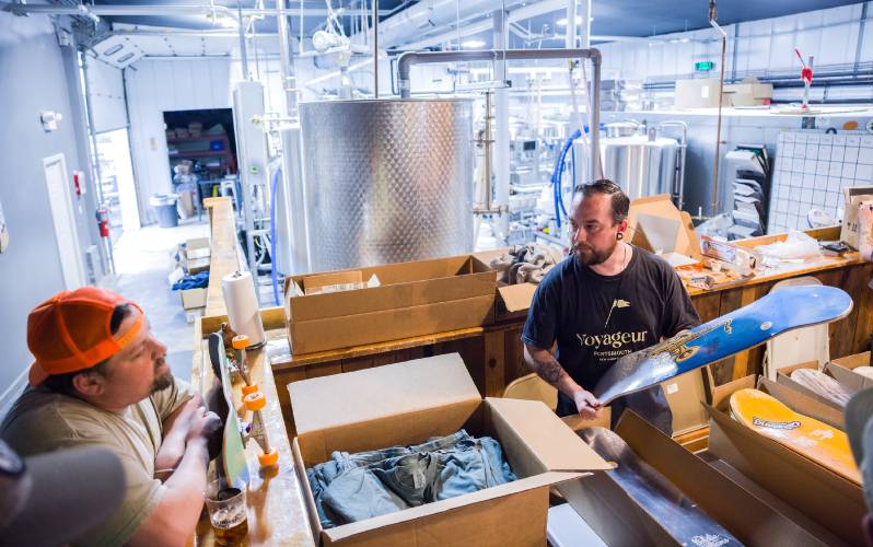 Tucker Jadczak, the owner of Feathered Friend Brewing Co., talks with Chris Harrington as he unpacks custom skateboards at the brewery during their market benefit event on Saturday, May 3, 2025. Due to the rain, most of the activities took place indoors.