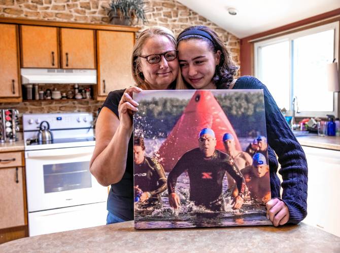 Maia Bradley and her mother, Miiko, hold up a photo of Mike Bradley in one of his triathlon photos in the family kitchen on Saturday.