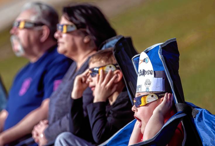 Axel Laperle (right), 6, looks up at the eclipse in the middle of a soccer field on the campus of NHTI in Concord with his cousin, Logan Lavoie and his grandparents, Lynn and Douglas Laperle as the light dimmed and it reached the maximum coverage on Monday.