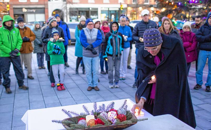 Bishop Robert Hirschfeld of the Episcopal Diocese of New Hampshire places a candle on a table at the City Plaza in front of the State House on Thursday in honor of one of the homeless persons that died in 2023.