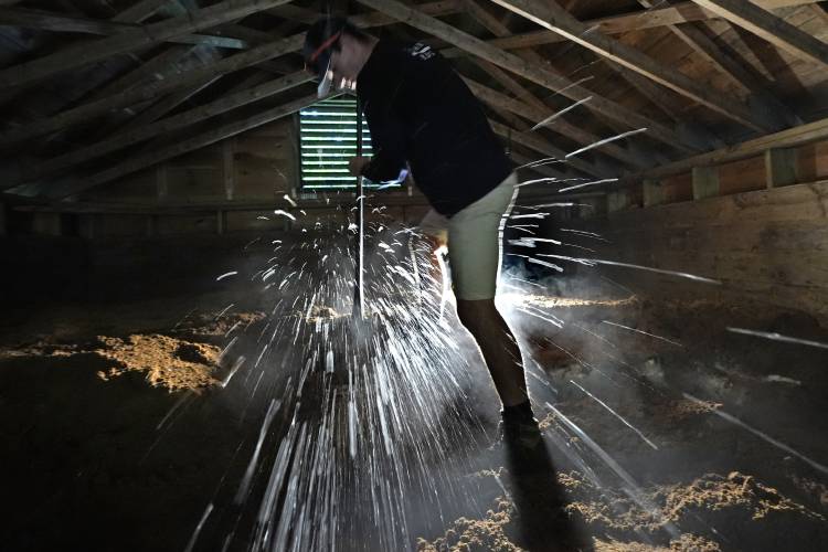 Ice chips fly as Nate Lord chops out a block at Rockywold Deephaven Camps, Thursday, June 20, 2024, in Holderness, N.H. Ice harvested from Squam Lake during the winter is insulated with sawdust in an ice house. It is used for refrigeration in ice boxes at each guest cabin throughout the summer. (AP Photo/Robert F. Bukaty)