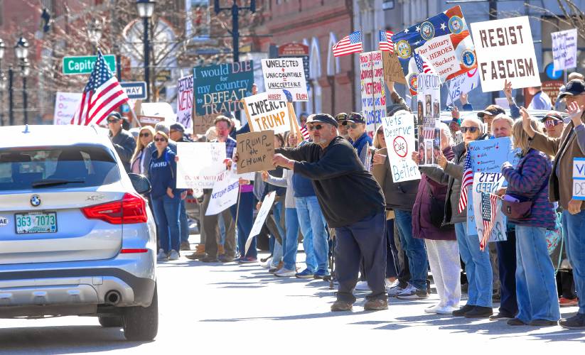 Disable veteran Dan Eleftheriou of Keene (center with black hat) holds up a sign as cars go by on Main Street in front of State House as hundreds protested for veterans rights on Friday.