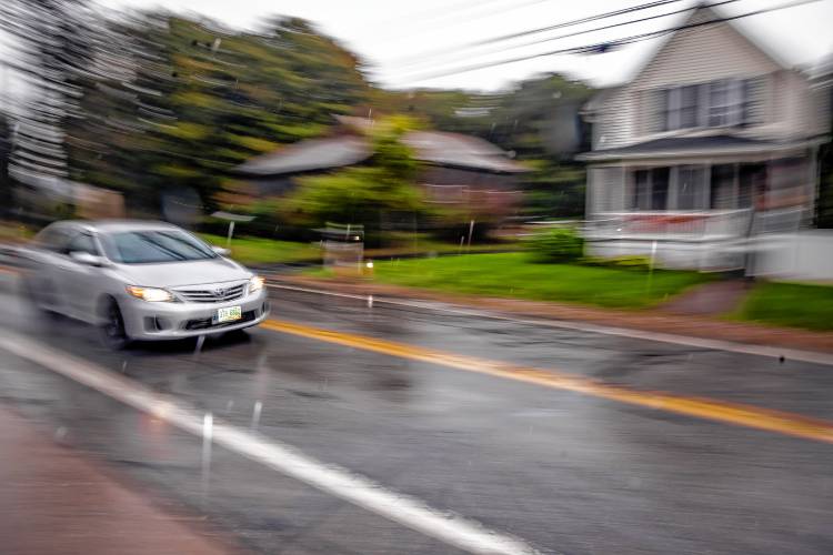 A car drives through the rain on Iron Works Road where drivers cut through from I-89.