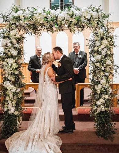 A bride and groom kiss while framed by a flower design.
