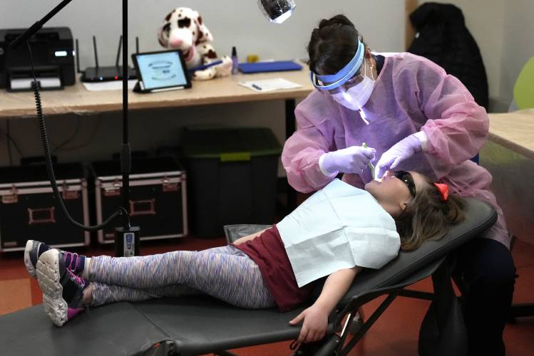 Dental hygienist Mary Davis examines Amber Warner's teeth at the Christa McAuliffe School in Concord in February. Mobile clinics provide critical dental access as do state programs that focus on preventive care and ensure dental care is incorporated into overall health efforts.