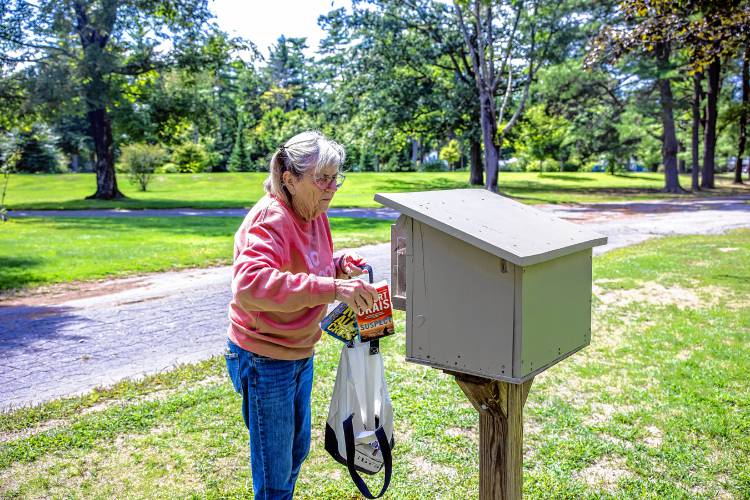 Mary McEvoy-Barrett puts books into the little library stand that she and her husband maintain at Rollins Park.