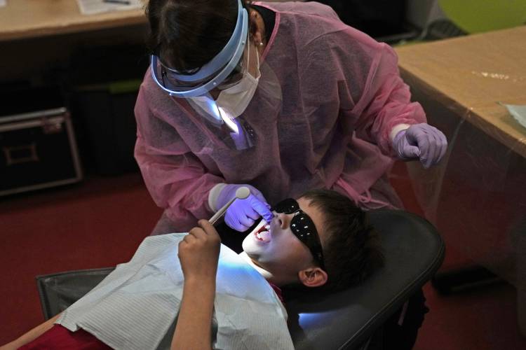 Clayton Warner holds a mirror as dental hygienist Mary Davis examines his teeth at the Christa McAuliffe School in Concord, N.H., Wednesday, Feb. 21, 2024. (AP Photo/Robert F. Bukaty) 