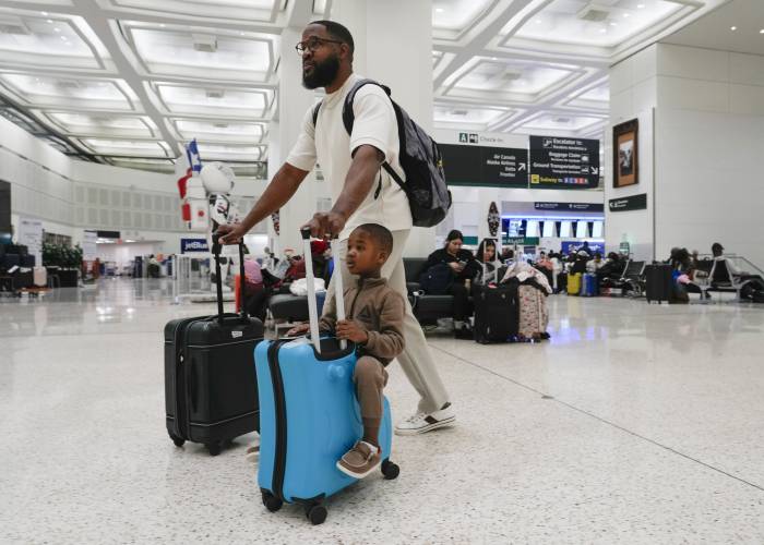 Rodney Onwu wheels luggage toward Southwest Airlines as his son, Micah, hitches a ride at George Bush Intercontinental Airport, Tuesday, Nov. 21, 2023, in Houston. (Jason Fochtman/Houston Chronicle via AP)