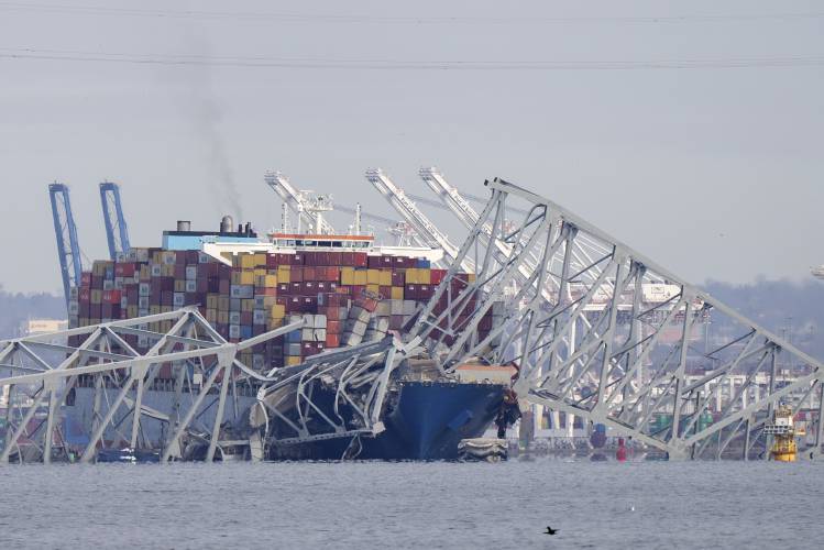 A container ship rests against wreckage of the Francis Scott Key Bridge on Tuesday, March 26, 2024, as seen from Pasadena, Md. The ship rammed into the major bridge in Baltimore early Tuesday, causing it to collapse in a matter of seconds and creating a terrifying scene as several vehicles plunged into the chilly river below. (AP Photo/Mark Schiefelbein)
