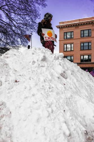 Lauren Winterholer of Rollinsford joined the hundreds of people by climbing up a snow mound at City Plaza in front of the State House on Monday.