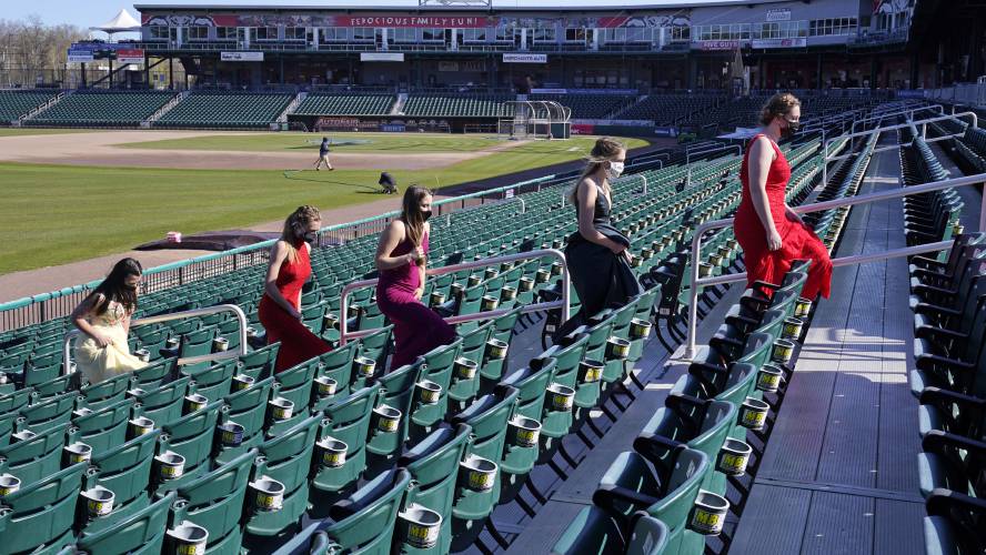 While wearing their prom gowns, students walk through the stands along the third baseline at the New Hampshire Fisher Cats minor league baseball stadium in Manchester, N.H., on Monday, April 26, 2021. After a year without proms, school districts across the country are debating whether they can safely hold an event that many seniors consider a capstone to their high school experience. The nearly 300 student senior class of Manchester's Central High School are waiting to get approval...