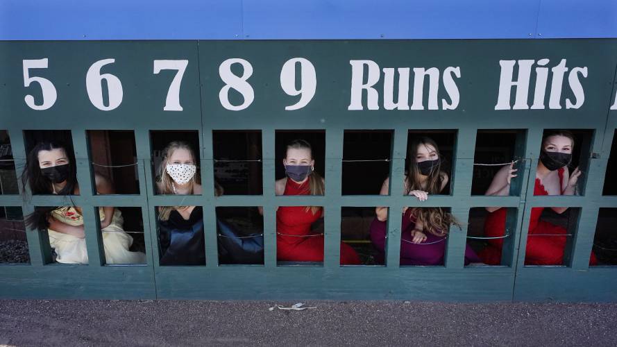 While wearing their prom gowns, students peer through the scoreboard at the New Hampshire Fisher Cats minor league baseball stadium in Manchester, N.H., on Monday, April 26, 2021. After a year without proms, school districts across the country are debating whether they can safely hold an event that many seniors consider a capstone to their high school experience. The nearly 300 student senior class of Manchester's Central High School are waiting to get approval from the city's board of health so they can have their prom at the outdoor venue, due to COVID-19 concerns. (AP Photo/Charles Krupa) 