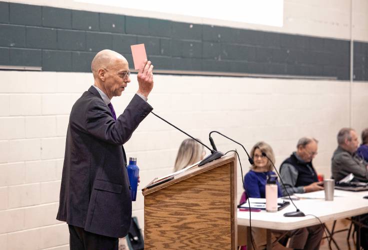 Henniker town moderator tells residents to pick up their voting card as they enter the Henniker Community School gym before the town meeting on Saturday, March 16, 2024.