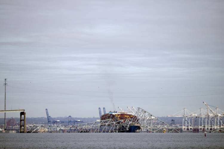 A container ship rests against wreckage of the Francis Scott Key Bridge on Tuesday, March 26, 2024, as seen from Pasadena, Md. The container ship rammed into the major bridge in Baltimore early Tuesday, causing it to collapse in a matter of seconds and creating a terrifying scene as several vehicles plunged into the chilly river below. (AP Photo/Mark Schiefelbein)