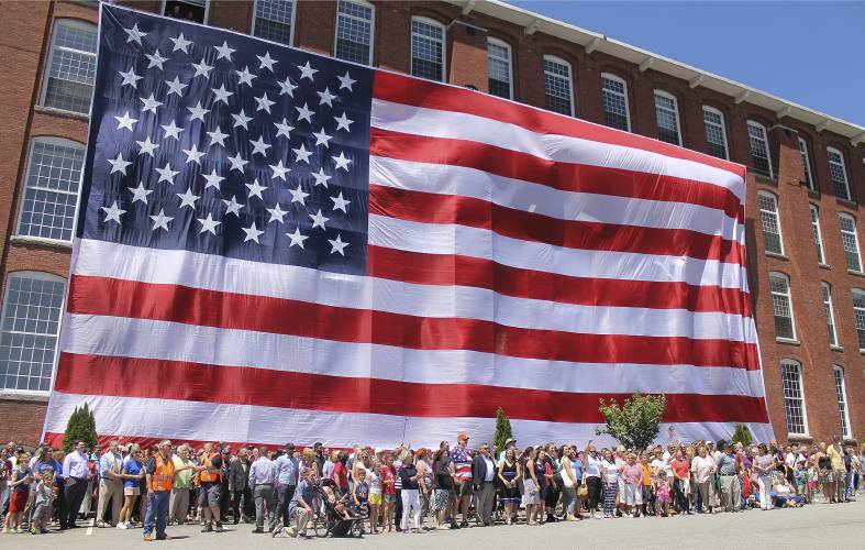People pose in front of an American flag outside a former textile mill building in Manchester. It replicated a photo taken in 1914 of workers at the Amoskeag Manufacturing Company with the original “Great Flag” they produced. 