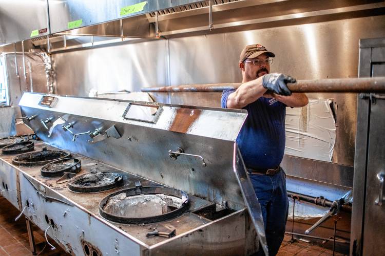Owner Adam Edwards of Edwards Plumbing, Heating and Air Conditioning takes out a gas pipe from a row of woks from the last tenant, a Chinese takeout restaurant,  as he works on the kitchen for The Forum Pub in the Thirty Pines plaza in Penacook on Thursday.
